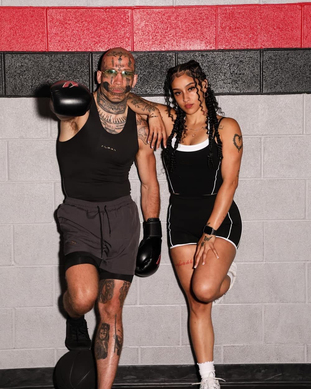 Two models in ALPHA black by the red boxing-gym wall